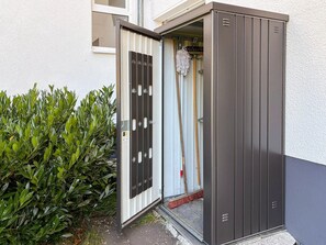 A metal security door with a handle and a keyhole, a mop leaning against it, and a green bush beside the door. - Modern Apartment Retreat for 6 in Winterberg Zuschen (Schmallenberg)