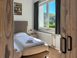 A bedroom with a bed, a nightstand, a lamp, a radiator, and a window with a view of greenery. - Modern Apartment Retreat for 6 in Winterberg Zuschen (Schmallenberg)