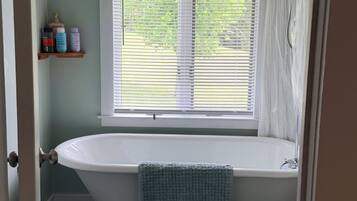 A bathroom with a bathtub, toilet, and window with blinds.
