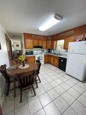 Una cocina con armarios de madera, un refrigerador blanco, una mesa de comedor con sillas y un microondas.
