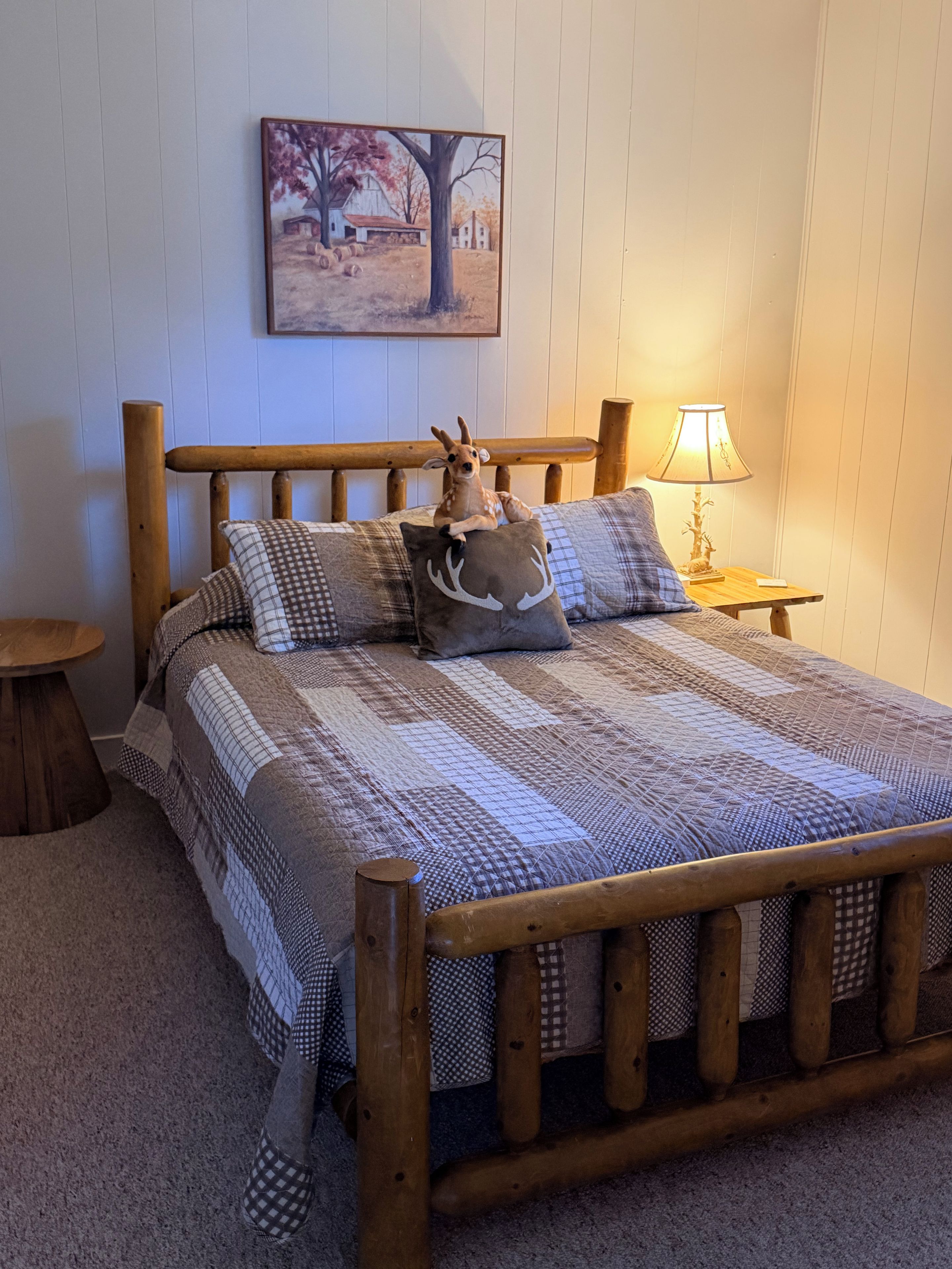 Un lit en bois avec une couvre-lit à motifs, un coussin orné d’un cerf et une lampe sur une table de chevet.
