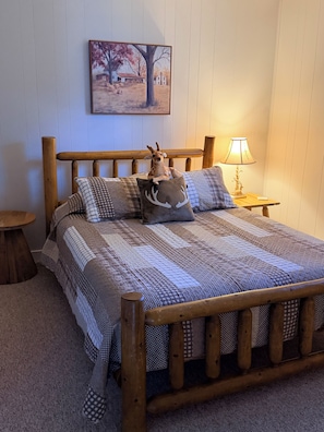 Un letto di legno con una coperta a motivi, un cuscino a forma di cervo e una lampada su un comodino.