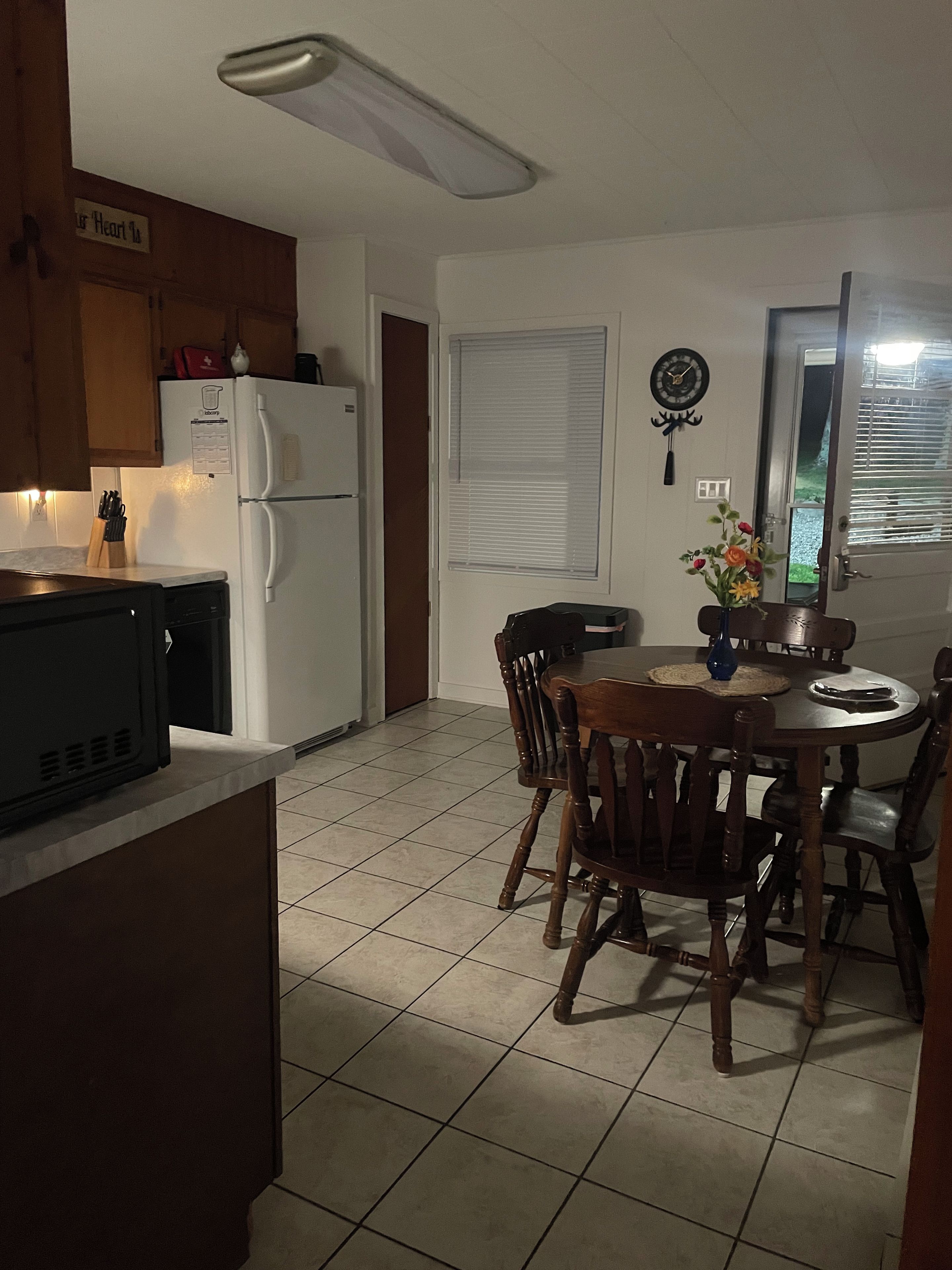 Una cocina con refrigerador, microondas y mesa de comedor con sillas.