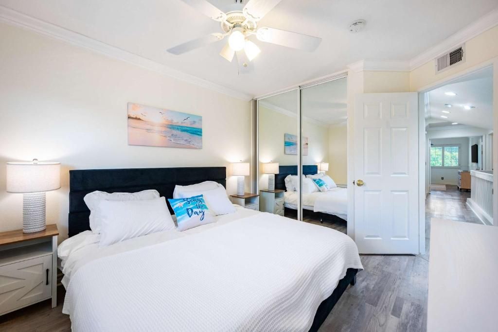 Een slaapkamer met een bed, nachtkastjes, een plafondventilator, een deur en een gang naar een andere kamer.