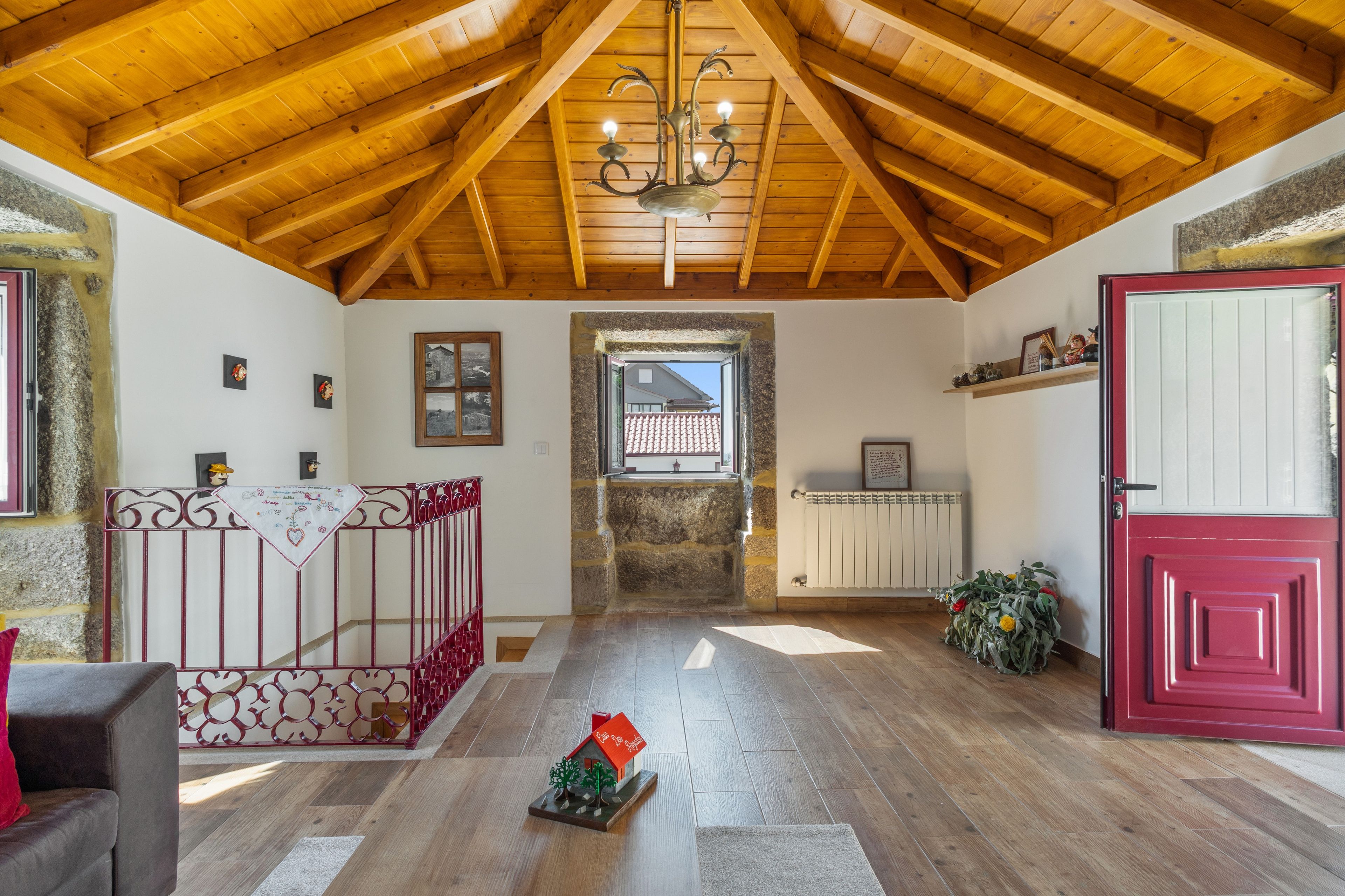 A room with a sloped wooden ceiling, a red crib, a small house model, and a red door.