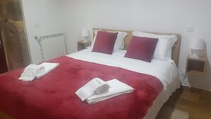 Un letto rifatto con cura, una coperta rossa e cuscini, un comodino bianco con una lampada e un termosifone sulla parete.
