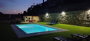 Piscina con pared de piedra y zona de patio con sillas.