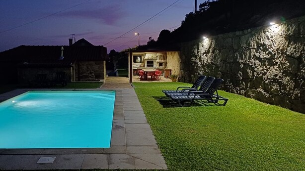 Una piscina con zona solarium, un'area barbecue e un muro in pietra.
