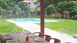 Area pranzo all'aperto con tavoli apparecchiati per un pasto, con vista su una piscina e un giardino curato.