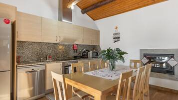 Una cocina con armarios de madera, encimera de granito, lavavajillas de acero inoxidable, una mesa de comedor de madera con sillas, una planta en maceta y un letrero colgante.