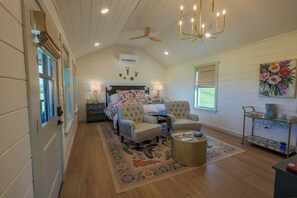 A spacious bedroom with a large bed, two armchairs, a small round table, and a ceiling fan.
