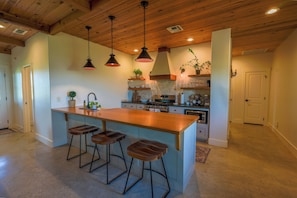 A modern kitchen with a wooden island, bar stools, pendant lighting, and a stone backsplash.
