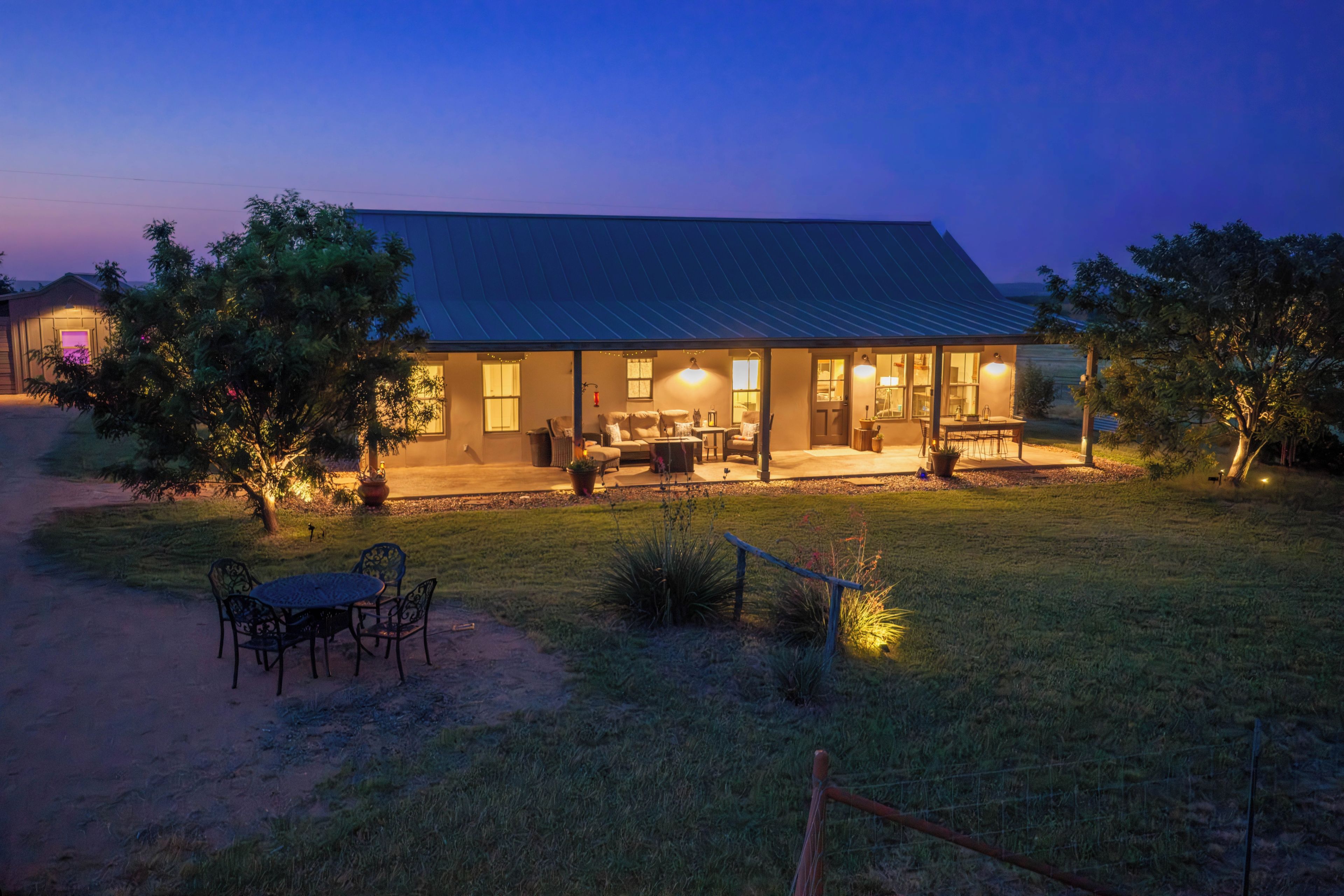 A two-story house with a covered patio, outdoor seating, and a well-lit entrance.
