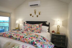 Une chambre à coucher avec une couvre-lit à motifs floraux, une tête de lit en bois, deux lampes de chevet, une table de chevet avec une lampe et des décorations murales représentant des têtes d’animaux.