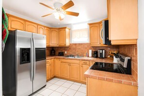 A kitchen with wooden cabinets, a stainless steel refrigerator, a black stove, and a ceiling fan. - Ocean Views. Golden Evenings. Unforgettable Stays. (Rincón)