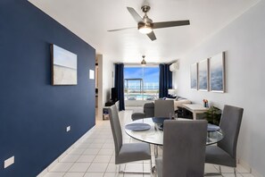 A modern hotel room with a balcony, a dining area with a glass table, and a ceiling fan. - Ocean Views. Golden Evenings. Unforgettable Stays. (Rincón)