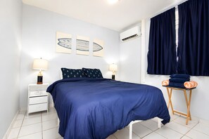 A bedroom with a bed, two bedside tables with lamps, a window with curtains, and artwork on the wall. - Ocean Views. Golden Evenings. Unforgettable Stays. (Rincón)