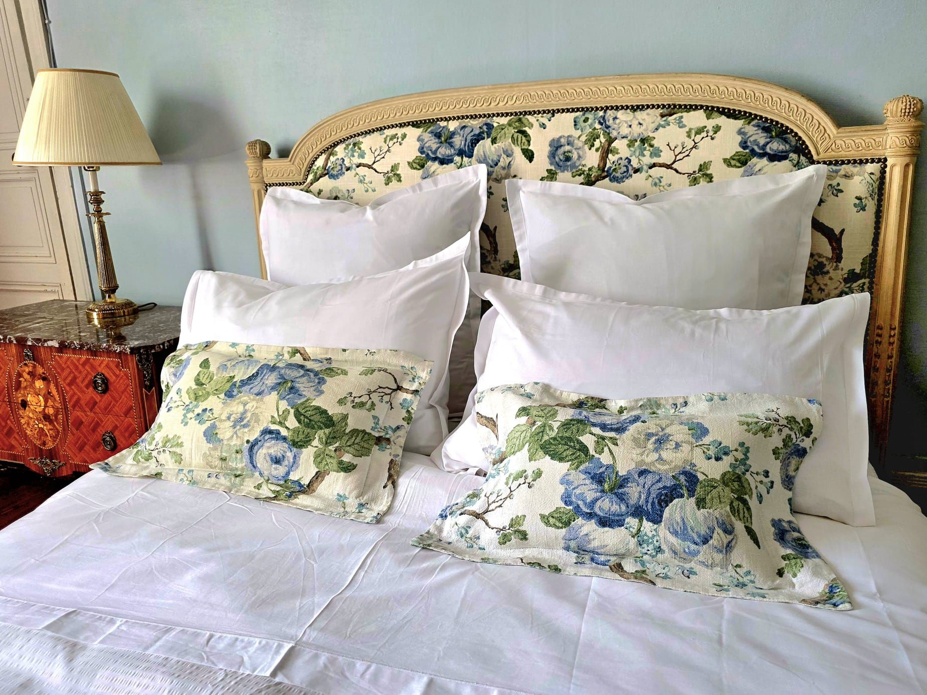A bed with white bedding and floral-patterned pillows.