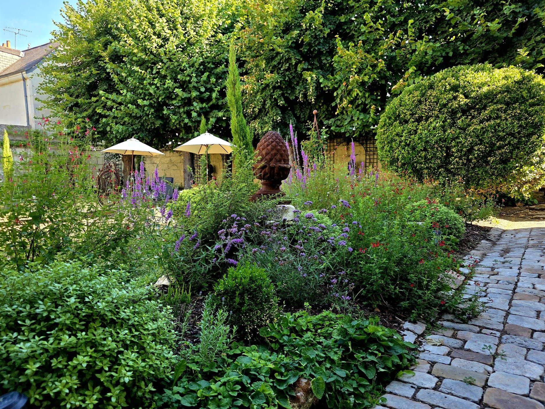 Un jardín con un sendero de piedra, diversas plantas y una estatua.