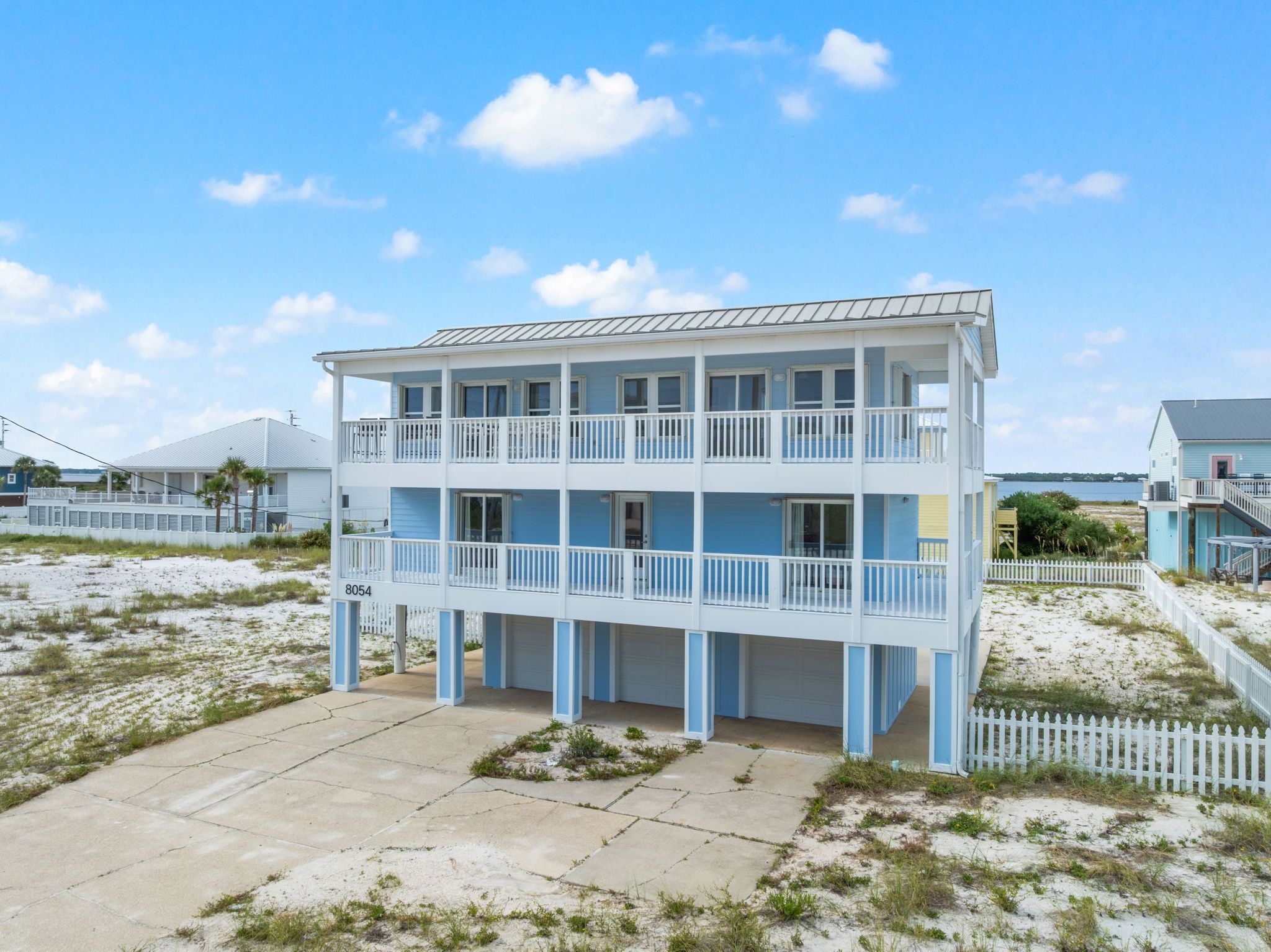 Een tweelaags gebouw aan het strand, met een balkon op elke verdieping, nummer 8054, en een witte picket hek om het terrein.