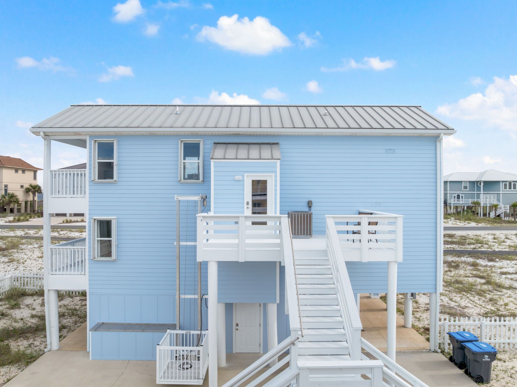 Een tweelaags strandhuis met een balkon, een klein portaal en een trap naar de bovenverdieping.