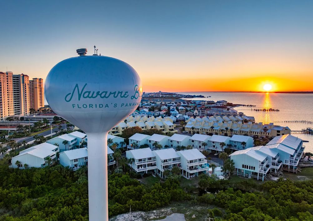 A view of a coastal area with a large water tower labeled 'Navarra's Florida's Panhandle' and a cluster of light-colored buildings with multiple stories.