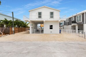 A two-story house with a balcony, a fenced yard, and a clear sky. - Oceanfront Marathon FL Home w/ Private Dock, Pool & Direct Ocean Access (Marathon)