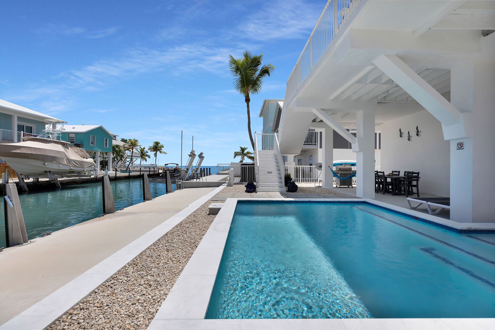A pool area with a clear blue pool, a staircase leading to a balcony, and a view of the ocean.