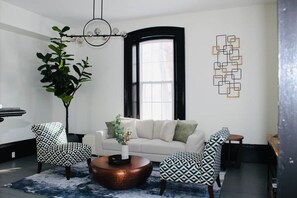 Ein modernes Wohnzimmer mit einer Couch, gemusterten Sesseln, einem Couchtisch und einem großen Fenster.