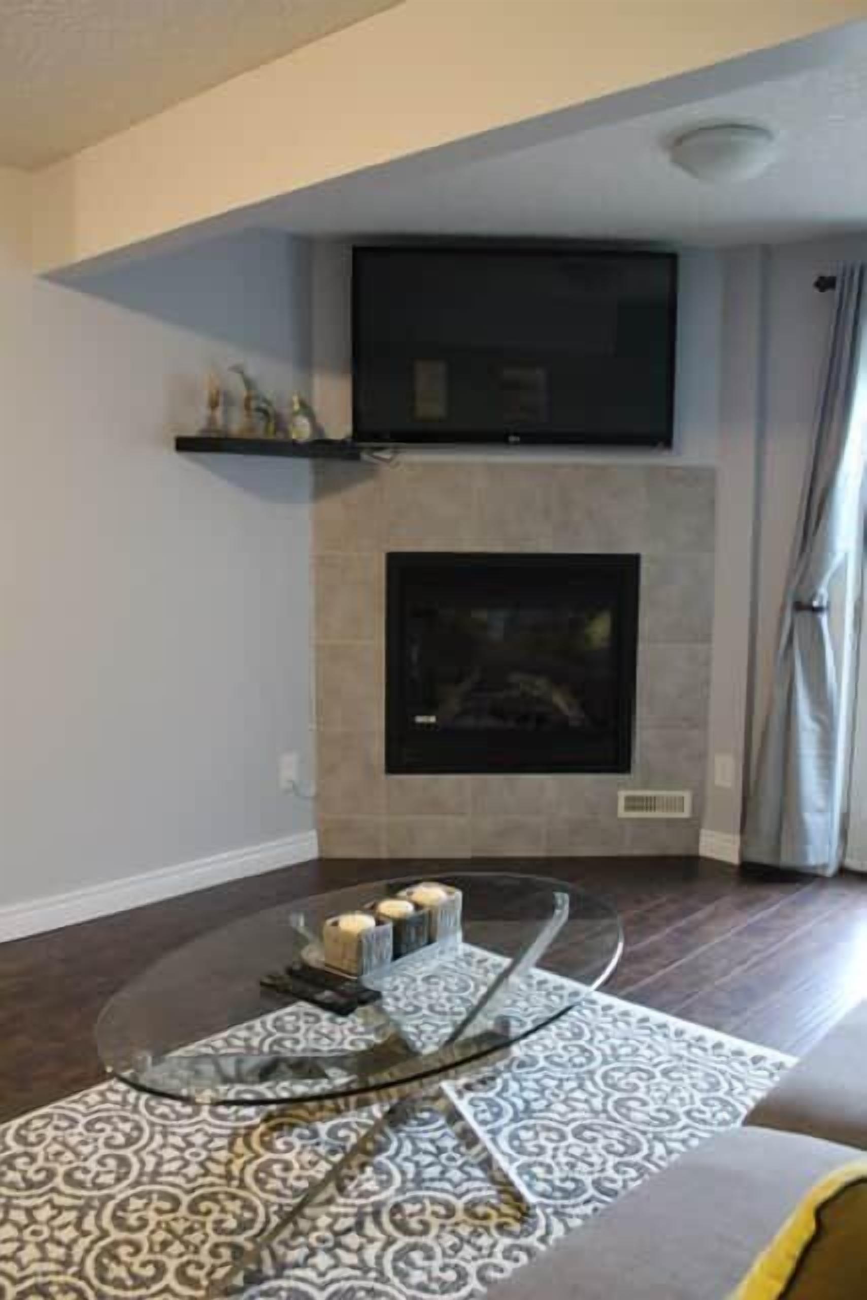 A living room with a fireplace, a flat-screen TV mounted above it, and a glass coffee table with candles.