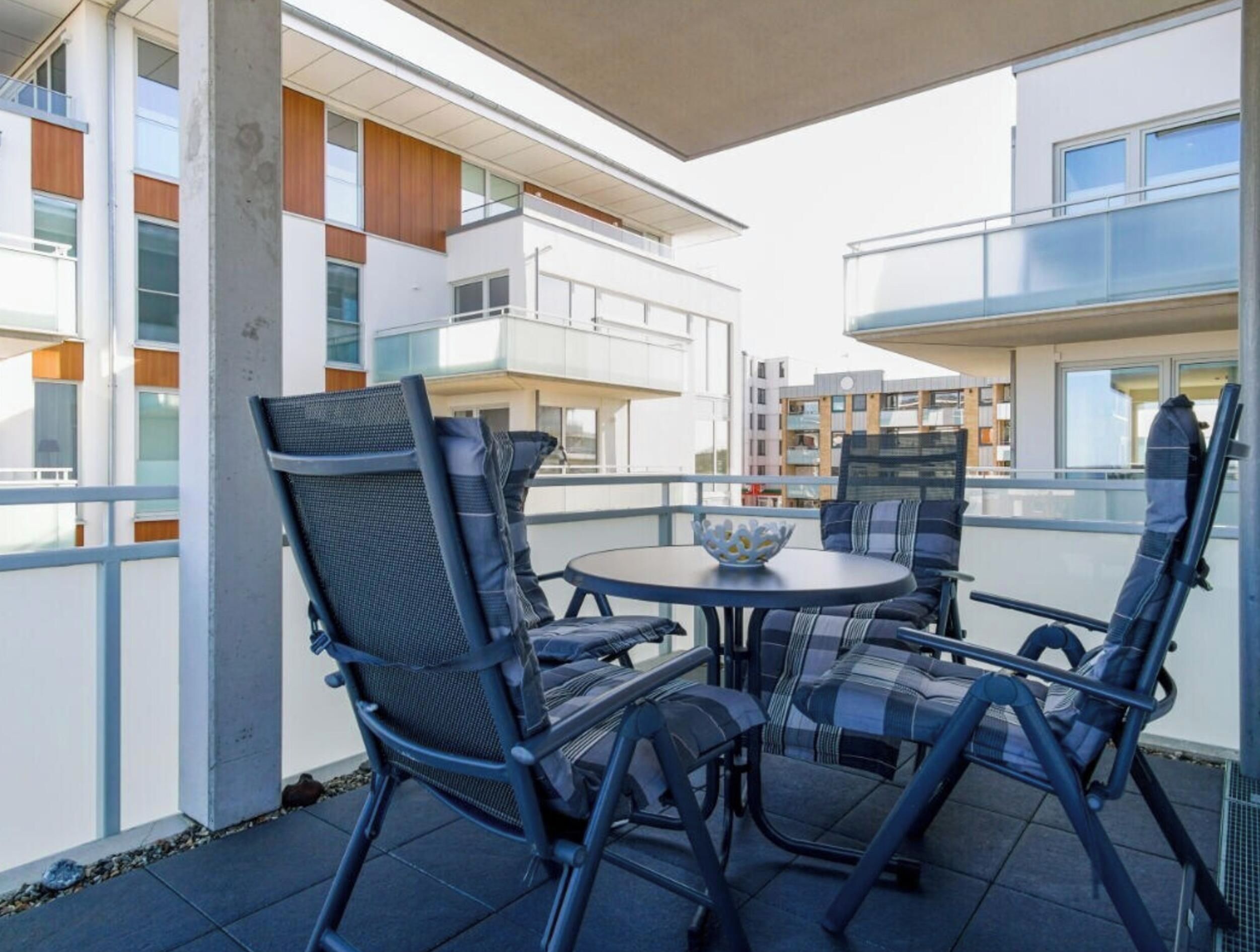Un espace extérieur aménagé avec des chaises et une table, offrant une vue sur un bâtiment moderne doté de balcons.