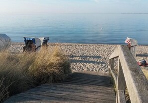 Een houten looppad dat naar een zandstrand leidt, met rustig water op de achtergrond.