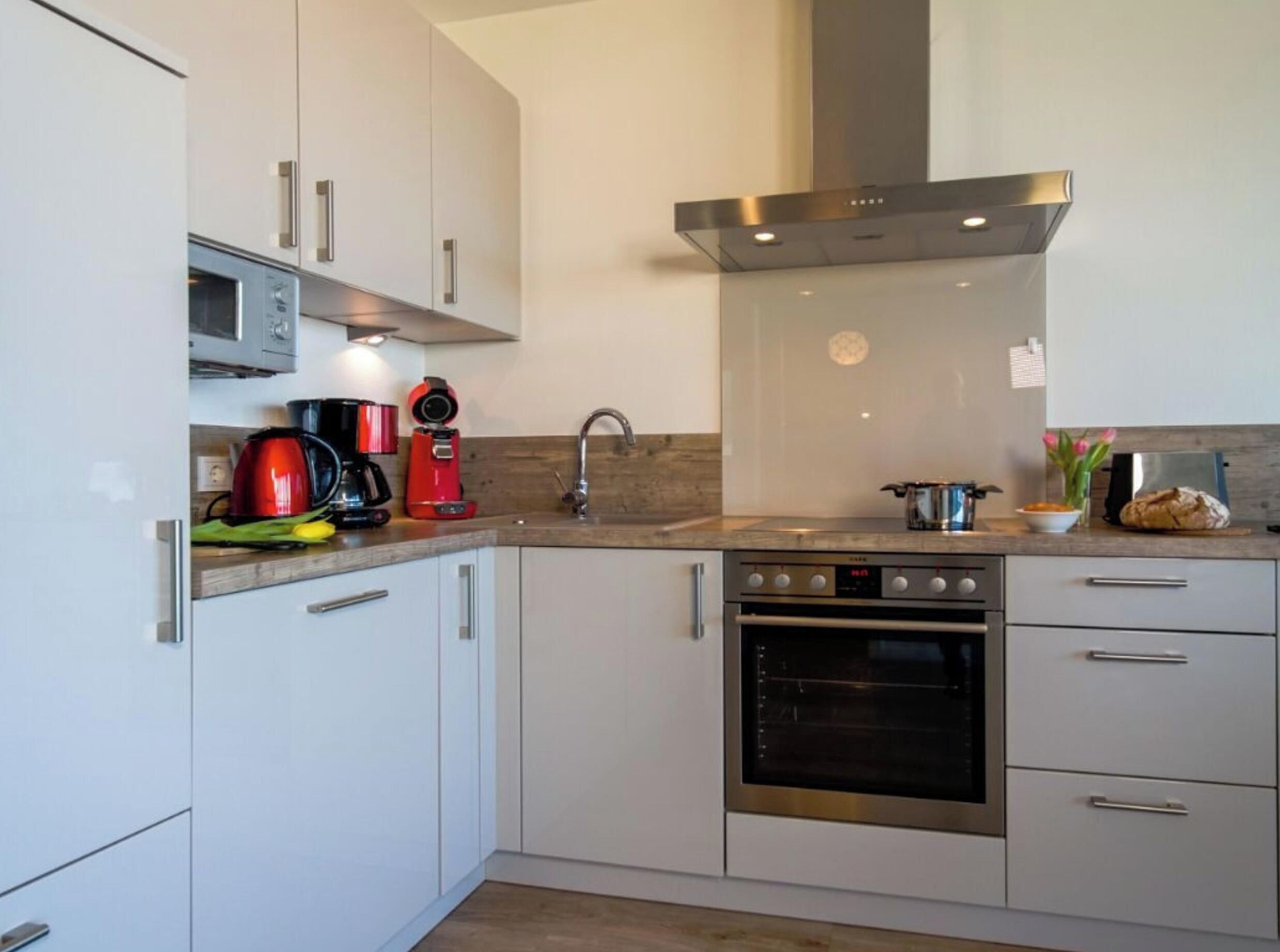 A modern kitchen with white cabinetry, a stainless steel range hood, a built-in oven, and a microwave.