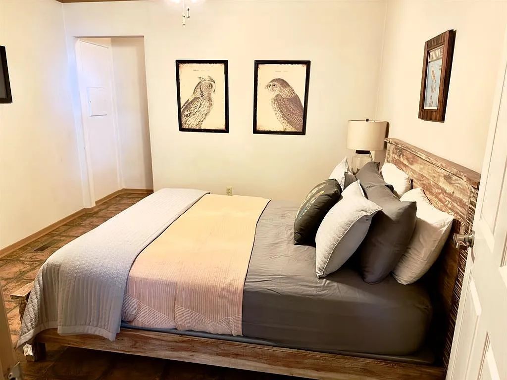 A bedroom with a bed, pillows, a bedside lamp, and two framed pictures on the wall.