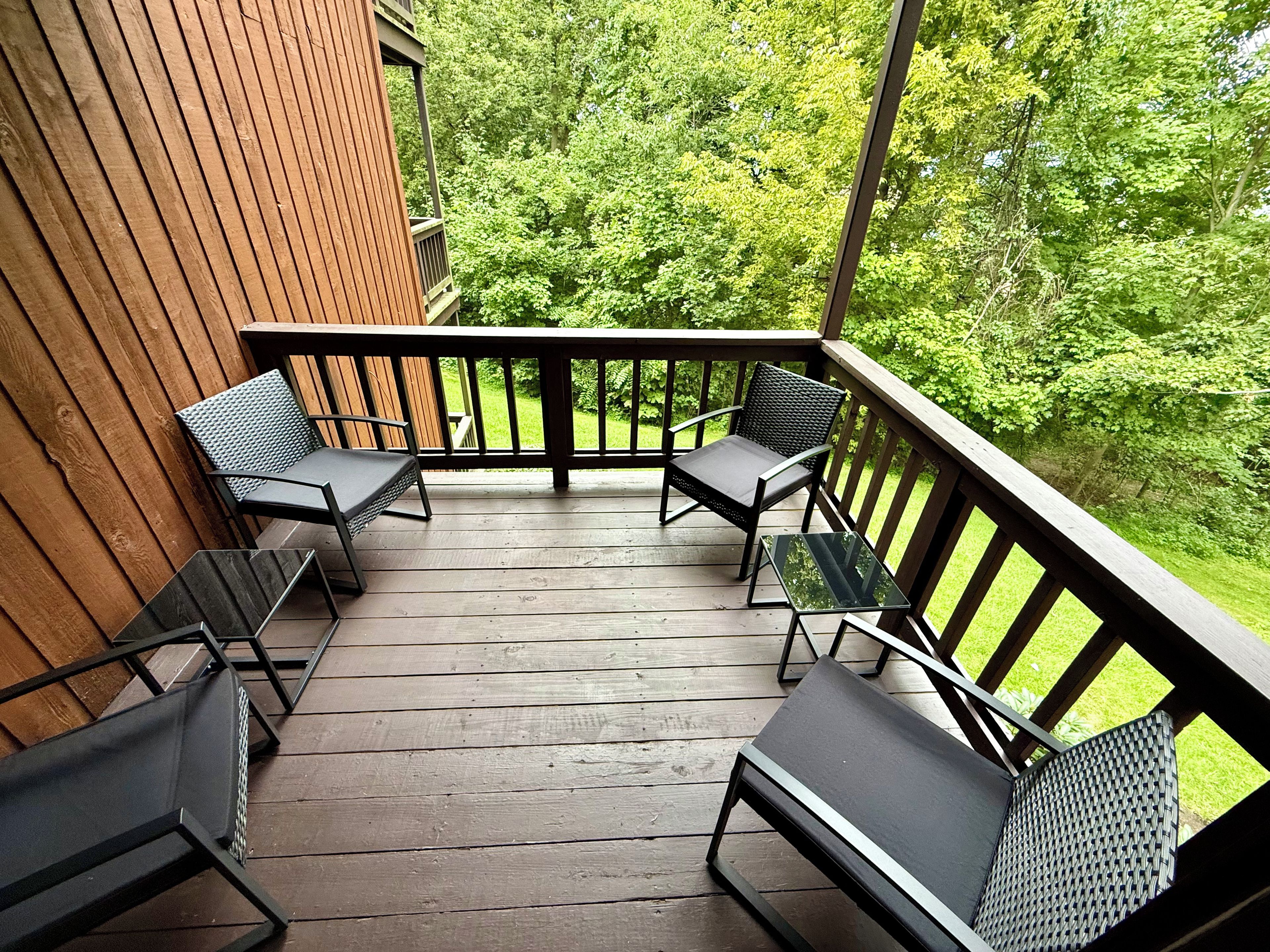 Une terrasse en bois avec quatre chaises et une table, entourée d’une balustrade en bois, d’où l’on peut admirer un paysage verdoyant et luxuriant.