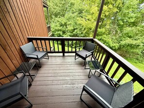 Una terraza de madera con cuatro sillas y una mesa, rodeada por una barandilla de madera, con vistas a un paisaje verde exuberante.