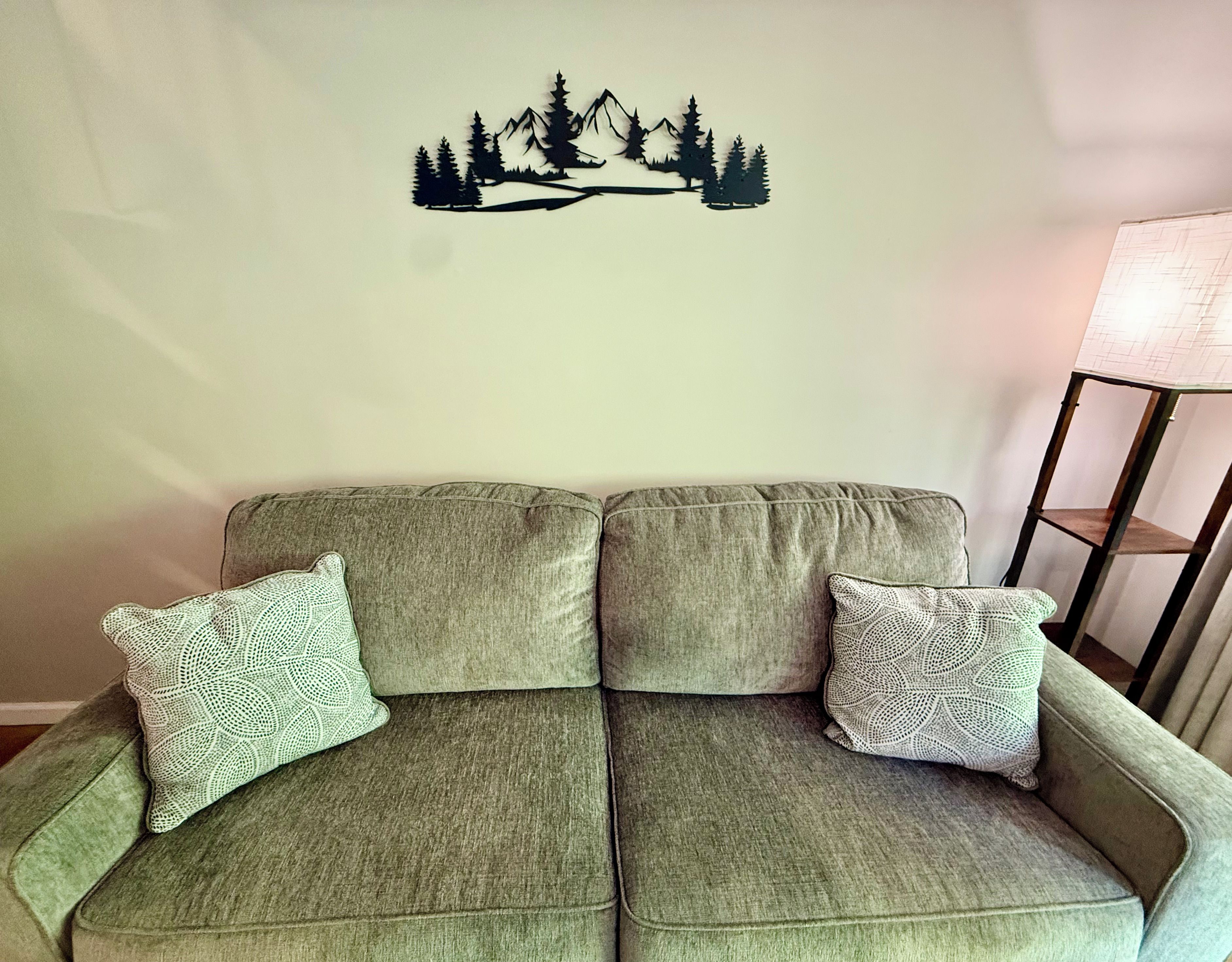 A two-seater sofa with patterned cushions against a wall with a mountain silhouette decal.