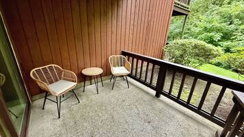 Un balcon avec deux fauteuils en osier et une petite table ronde, une balustrade en bois et une vue sur la verdure.
