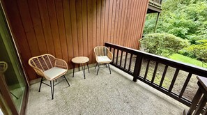 A balcony with two wicker chairs and a small round table, wooden railing, and a view of greenery. - Cozy 2 bedroom 2 bathroom with game room right in the Mountains of Vernon, NJ (Vernon Township)