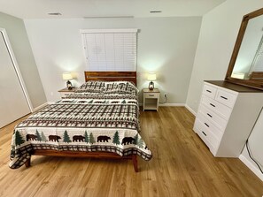 A bedroom with a wooden bed, a nightstand, a dresser, a mirror, and a window with blinds.
