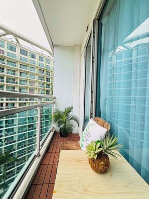 Ein Balkon mit einem Holztisch, einem Korbwäscher mit einer Pflanze und einem Kissen.