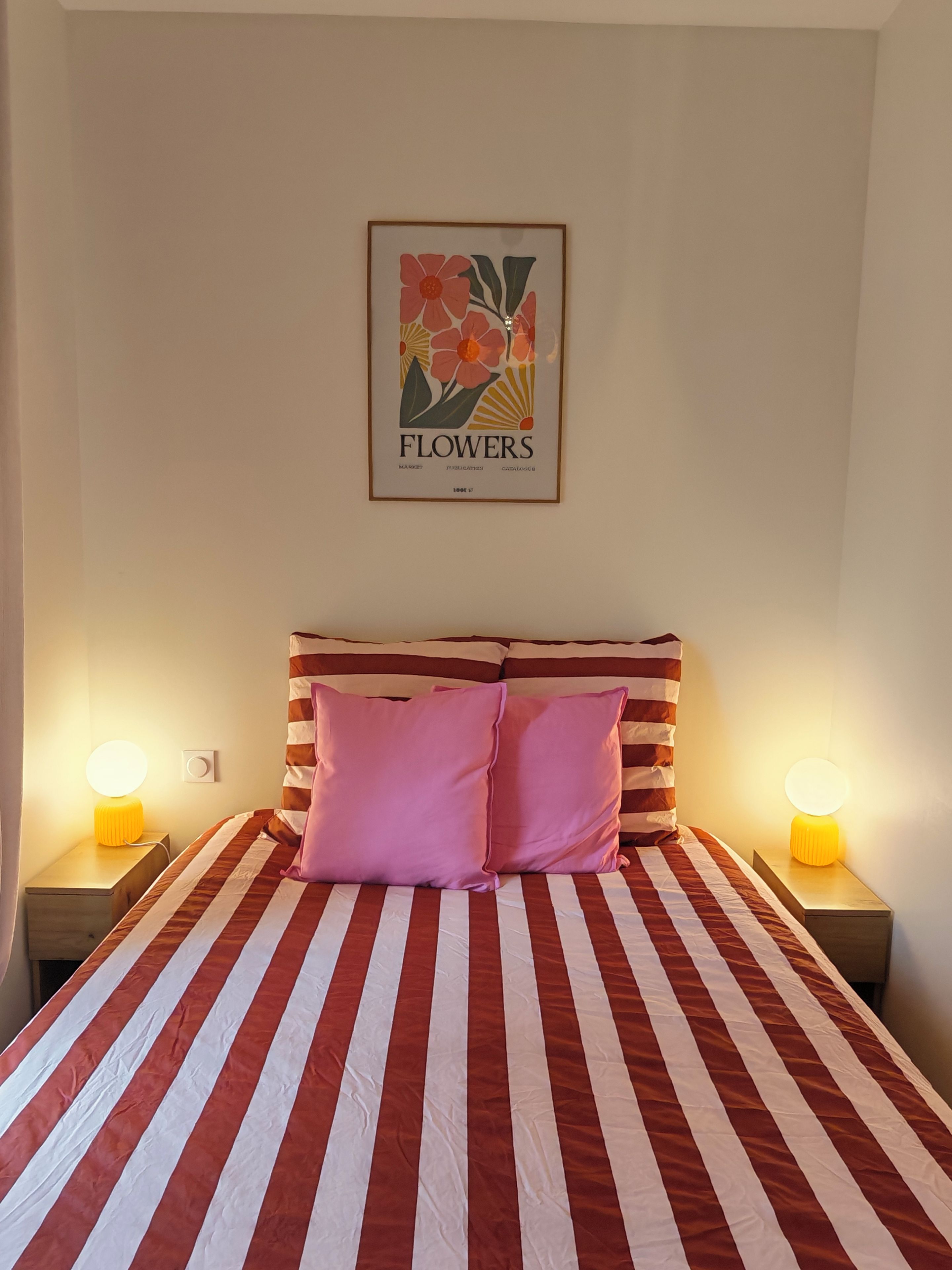 Ein Bett mit roten und weißen Streifen, zwei Nachttischlampen und ein gerahmtes Bild von Blumen an der Wand.