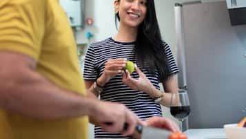 A person preparing food in a kitchen with a modern design, including a stainless steel refrigerator and a countertop with a bowl and a tomato.