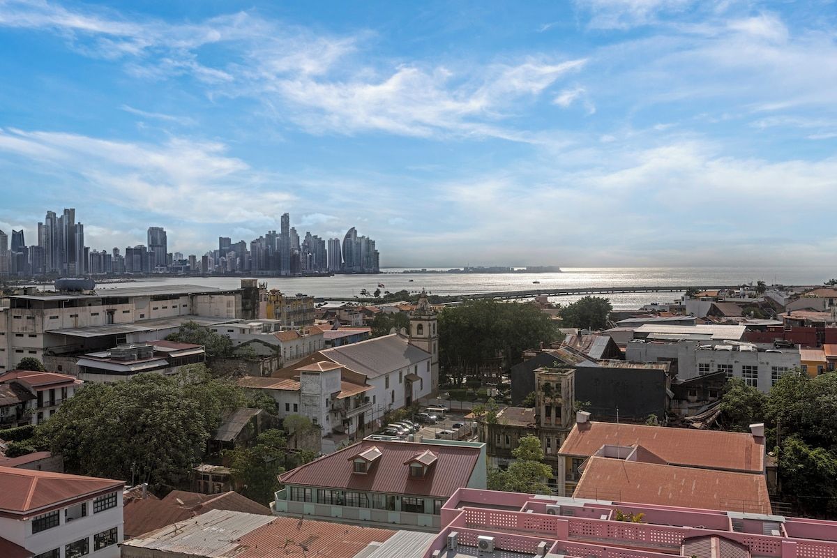 Un paisaje urbano costero con una mezcla de edificios modernos y tradicionales, cielo despejado y vista al mar.
