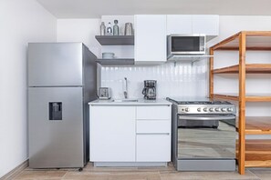 Une cuisine compacte équipée d’un réfrigérateur, d’un four à micro-ondes, d’une cuisinière et de meubles de rangement blancs.
