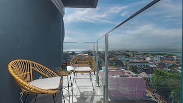 A balcony with wicker chairs and a glass railing overlooking a cityscape.