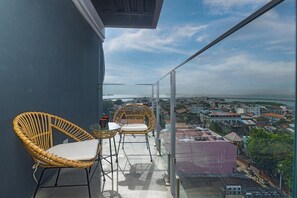 Un balcon doté de fauteuils en osier et d’une rambarde en verre, offrant une vue sur le paysage urbain.