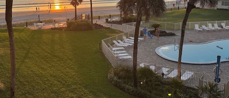 A pool area with lounge chairs and a view of the sunset over the ocean.
