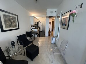 Un salon moderne avec une table basse en verre, des fauteuils noirs, un fauteuil transparent et un coin repas avec une table et des chaises blanches.
