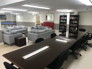 Ein Konferenzraum mit einem langen Tisch, zwei Sofas, einem roten Klavier und einem Bücherregal voller Bücher.